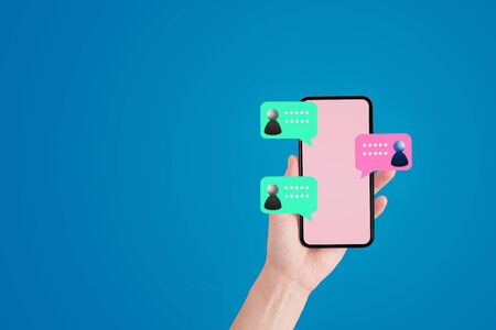 Social Networking and Business Communication Concept : Hand holding smartphone with speech balloon icons chatting together.の写真素材