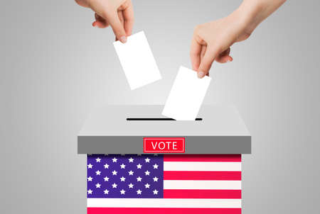 US Elections Concept : Hand holding and putting voting paper in ballot voting box with USA flag...