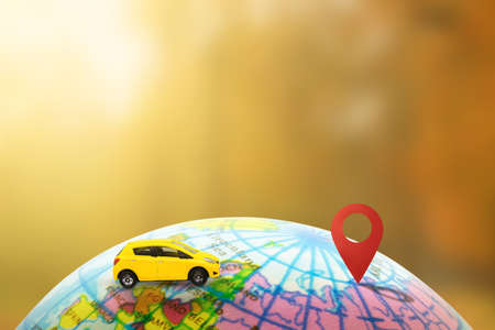 Travel and Car Trip Concept : Yellow model toy on globe running to destination checkpoint with sunlight in background.の写真素材