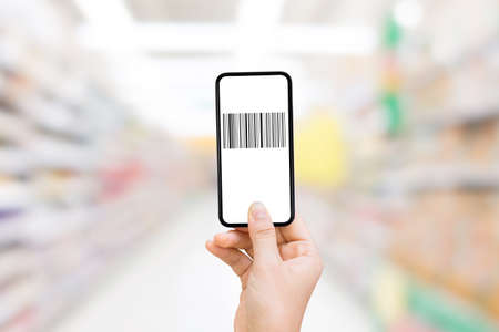 Shopping and Retail Concept  Hand holding smartphone that showing barcode on white screen and blurry image of supermarket in background.の写真素材
