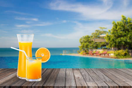 Summer Travel Trip Concept : Welcome drink orange juice punch put on wooden table nearly swimming pool with blue water and blue sky in background.の写真素材
