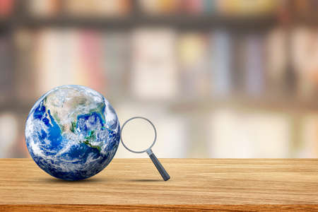 Learning and Education Concept : Magnifying glass lean on blue planet earth with blurry image of library room in background.の写真素材