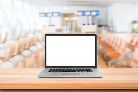 Laptop on wooden desk with blurry image of gate terminal departure airport in background.の写真素材