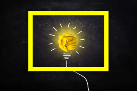 Business Idea Concept : Yellow crumpled paper ball light bulb lighting grow around on chalkboard in...