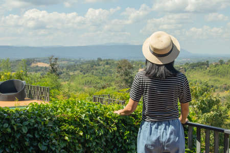 Asian woman wear weave hat and stand on wooden terrace. She feeling relax and happiness. she look at...