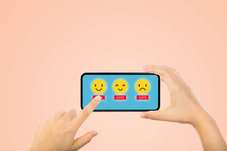 Customer Feedback Concept : Hand choosing yellow smile emotional icons for giving best service ranking on smartphone.の写真素材