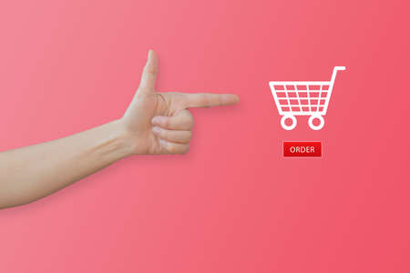 Shopping Online Concept : Hand gesturing and pointing to shopping cart icon on pink background.