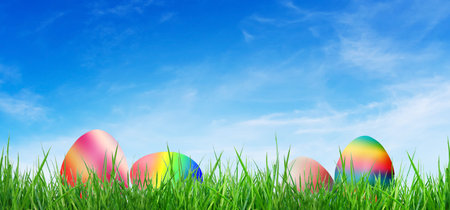 Group of Pastel colorful Easter eggs on green grass with blue sky in background.