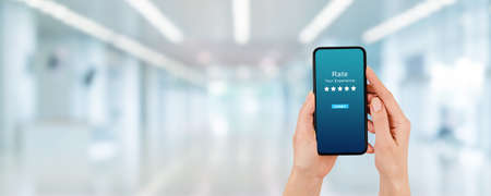 Customer Feedback Concept : Hand holding smartphone and giving best service ranking in blurred...