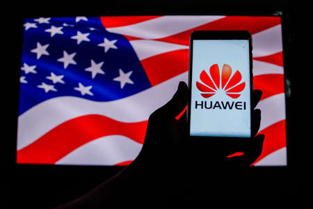 PERAK, MALAYSIA - MAY 24, 2019: A man holds an android-smartphone that shows the Huawei logo in front of the USA flag. Google is restricting Huawei's access to its Android system.のeditorial素材