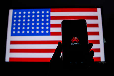PERAK, MALAYSIA - MAY 24, 2019: A man holds an android-smartphone that shows the Huawei logo in front of the USA flag. Google is restricting Huawei's access to its Android system.のeditorial素材