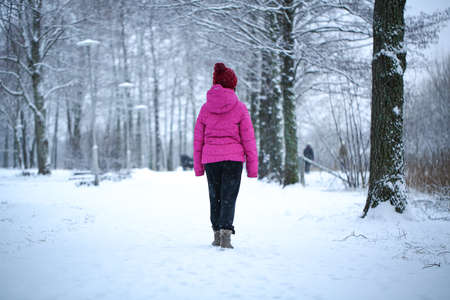 Young asian girl with a pink jacket walks on a snowy road