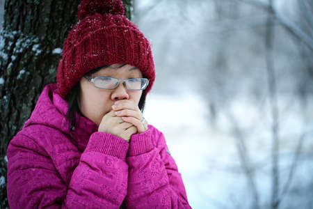 Young and moody asian girl with a pink jacket leaning against a tree in the winterの写真素材