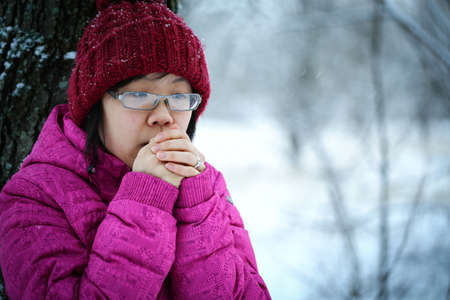 Young and moody asian girl with a pink jacket leaning against a tree in the winter