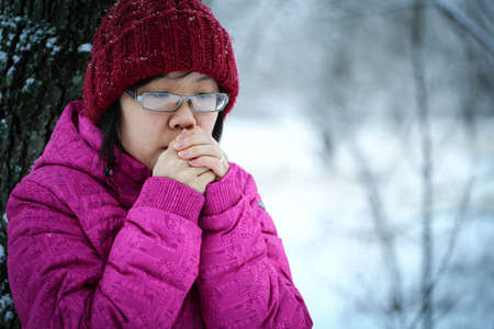 Young and moody asian girl with a pink jacket leaning against a tree in the winterの写真素材