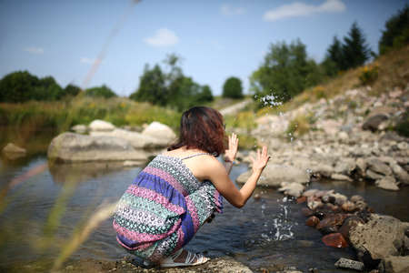 Young asian girl in a colorful maxi dress playing by a river in the summer