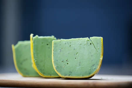 Dutch pesto cheese slices on a wooden background in a closeup view.の写真素材