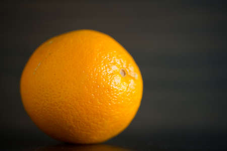 Single orange in front of a wooden background in a closeup view.の写真素材
