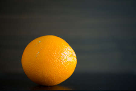 Single orange in front of a wooden background in a closeup view.の写真素材