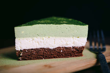 A piece of matcha/green tea, coconut powder, and chocolate cake in a closeup view.の写真素材