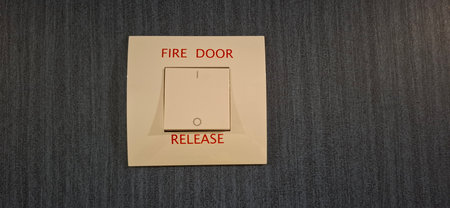 A close-up of a fire door release button mounted on a blue textured wall, emphasizing fire safety mechanisms in public or private facilities.の写真素材