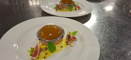 A close-up of plated dessert featuring caramel glaze, passion fruit sauce, fresh figs, and mint leaves, elegantly presented on white plates.の写真素材