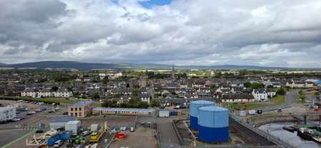 invergordon united kingdom aug 9 2024 A view of a town combining residential and industrial areas, set against rolling hills under a dynamic sky. The townscape highlights diverse land use and picturesque scenery.の写真素材