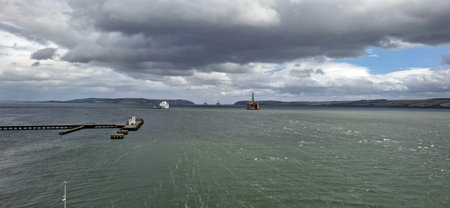 invergordon unitrd kingdom aug 9 2024 A dramatic seascape featuring a long pier, a visible ship, and offshore platforms under cloudy, expansive skies.の写真素材
