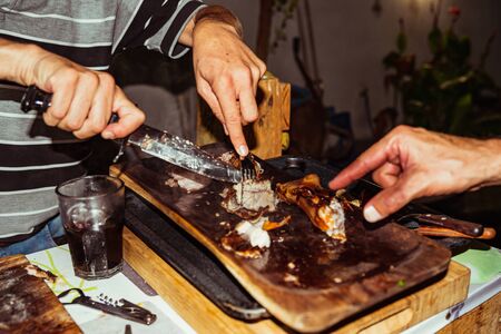 Chef hand cuts piece grilled pork in steaks with knife. Traditional suckling pig cooked on the charcoal grill. The little pig is roasted whole on an open fire. Organic pig on the spit.の写真素材