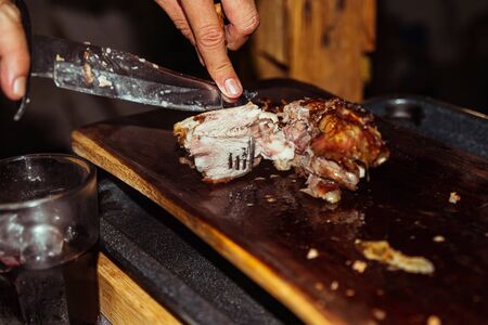 Chef hand cuts piece grilled pork in steaks with knife. Traditional suckling pig cooked on the charcoal grill. The little pig is roasted whole on an open fire. Organic pig on the spit.の写真素材