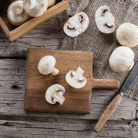Fresh Raw Mushrooms Champignons on a Wooden Cutting Board on Old Rustic Wooden Table Background Top viewの写真素材