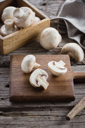 Fresh Raw Mushrooms Champignons on a Wooden Cutting Board on Old Rustic Wooden Table Backgroundの写真素材