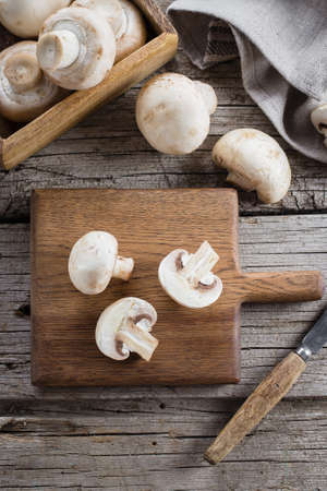 Fresh Raw Mushrooms Champignons on a Wooden Cutting Board on Old Rustic Wooden Table Background. Top viewの写真素材