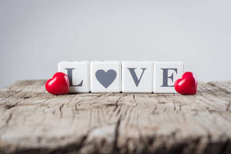 Valentine Day Card Concept. Creative Idea. Love message written in wooden blocks and ceramic red heart on old wooden background.の写真素材