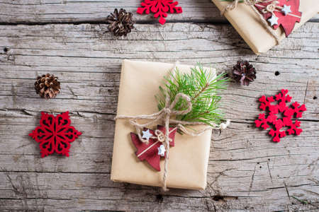 Holiday christmas gift box. Christmas present with fir branch and red wooden tree toy decoration on wooden table background. Top view, copy spaceの写真素材