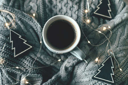 Cozy, mood, lifestile, still life concept. Mug of coffee, sweater and garland lights on gray knitted sweaters as background. Christmas or New Year 2020 holiday concept. Top view, flat lay, closeupの写真素材