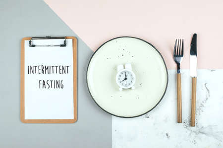 Intermittent fasting, ketogenic, diet concept. Empty plate with white alarm clock and white note notepad on blue background. Flat lay, top viewの素材 [FY310133673767]