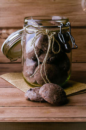 Chocolate Cookies on Paper in Glass Jar on Wooden Table Background. Sweet Snack. Copy spaceの写真素材