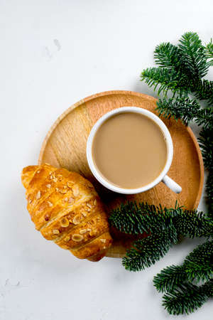 Christmas breakfast. Cup of coffee, croissant and holiday decoration toys, tree fir branches on white table. background. Top view, flat layの写真素材