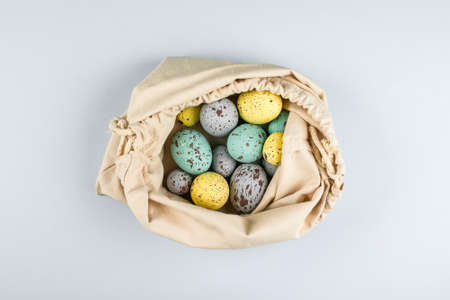 Zero Waste Easter concept. Colorful pastel easter eggs in textile bag on grey background. Top view,...