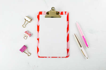 Flat lay fashion feminine home office workspace with blank paper clipboard, pens and clips on white table background. Top view. copy space. Mockup conceptの写真素材