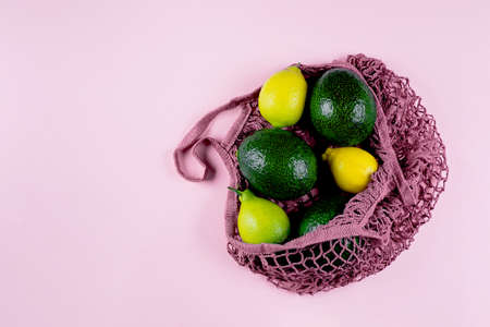 Mesh shopping bag with lemons and avocado on pink background. Top view, flat lay, copy space. Zero waste, eco friendly concept.の写真素材