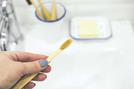 Bamboo wooden toothbrush in woman's hand in bathroom interior. No plastic, zero waste concept. Eco...