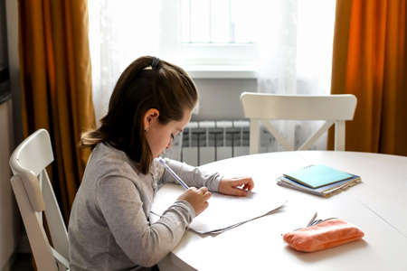 Pretty cute schoolgirl 7-8 years old studying at home. Home school, online education, home education, quarantine, coronavirus conceptの写真素材