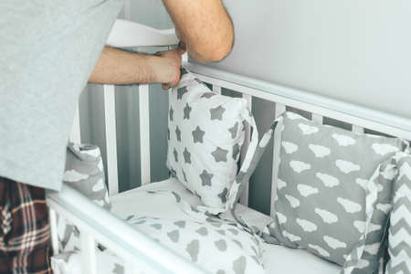 Father helps young mother put on bumpers in the crib. Family lifestyle concept
