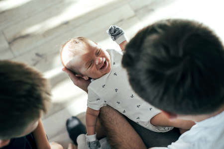 Father's hand hugging cute newborn son. Little happy smiling baby with father and brother. Home...