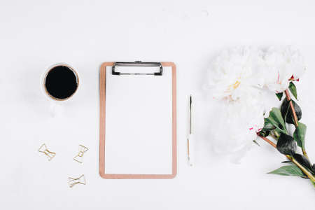 Office table desk. Workplace with cup of coffee, flowers peonies, pen, clipboard. Flat lay, top...