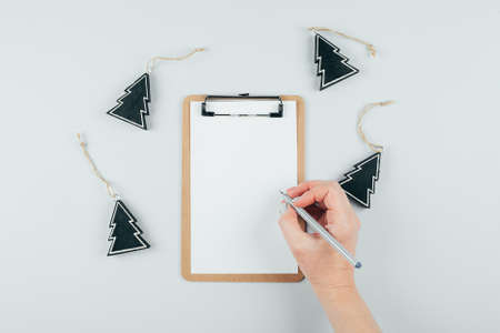 Flat lsy with christmas holiday decor. Woman hands holding paper sheet or notebook and pen. Gray...