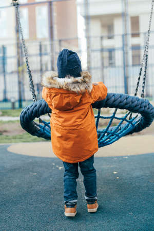 Little boy 5 years old in an orange jacket at the playground. Children's leisure outdoors, games on the street.の写真素材
