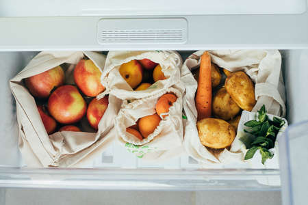 Zero waste concept. Fresh vegetables and fruits in eco cotton bags (tote bag) in a refrigerator from...